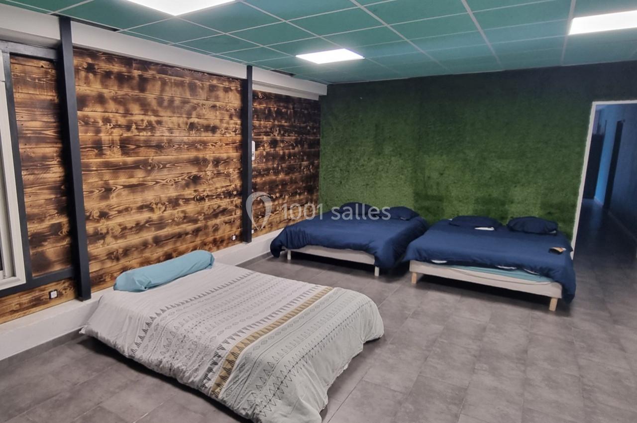 Trois lits dans une pièce avec mur en bois, mur vert texturé, plafond à dalles et sol en carrelage gris.