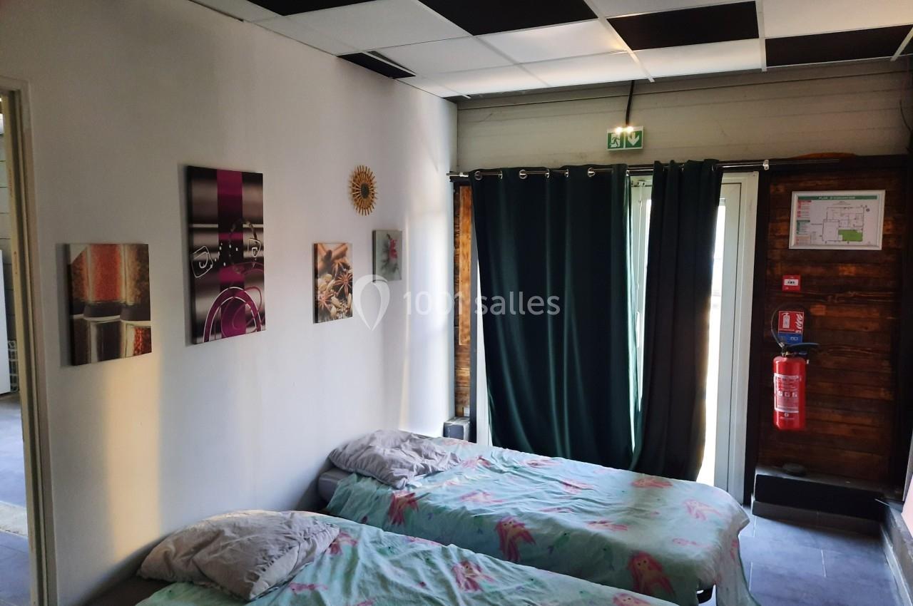 Deux lits simples avec des draps colorés dans une pièce lumineuse, décorée de tableaux et équipée de rideaux sombres.