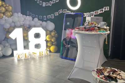 Décoration d'anniversaire avec ballons, chiffres lumineux ’18’, miroir interactif et accessoires sur une table.