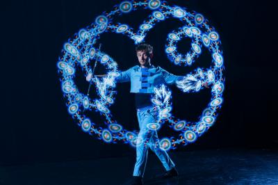 Un jongleur manipule des bâtons rouges dans une galerie lumineuse avec une verrière en arrière-plan.