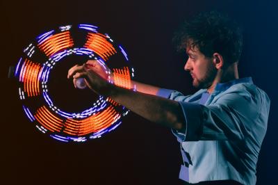 Un jongleur manipule des bâtons rouges dans une galerie lumineuse avec une verrière en arrière-plan.