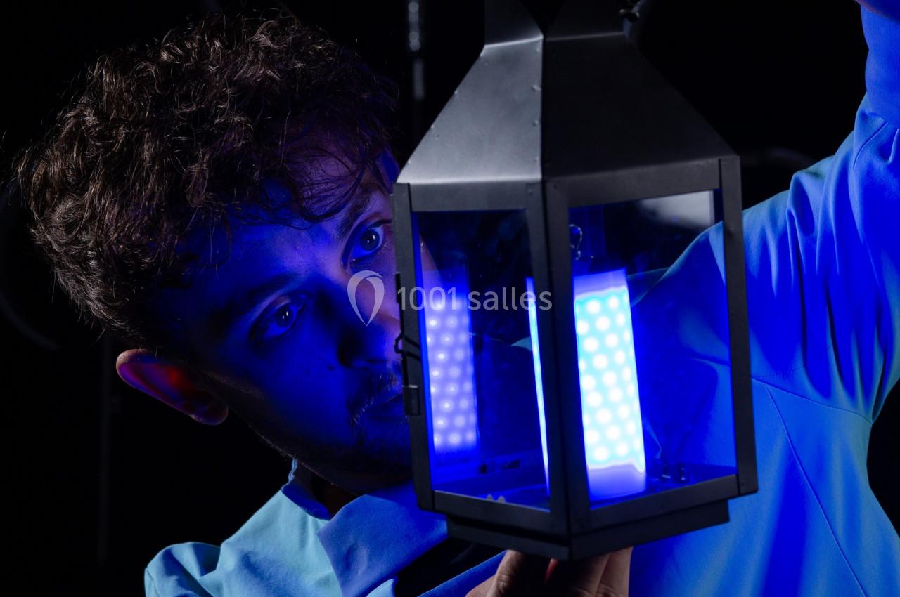 Un homme examine une lanterne noire émettant une lumière bleue vive dans un environnement sombre.