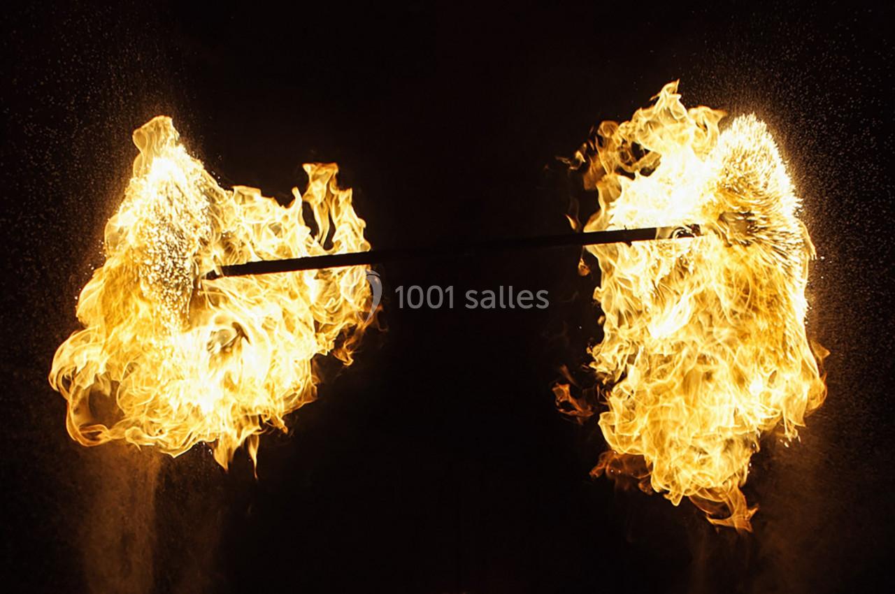 Deux torches enflammées fixées à une barre métallique, entourées d'étincelles dans un environnement sombre.