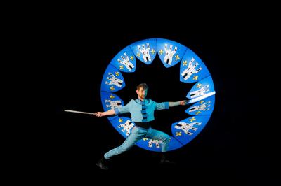 Un jongleur manipule des bâtons rouges dans une galerie lumineuse avec une verrière en arrière-plan.