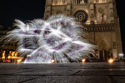 Un jongleur manipule des bâtons rouges dans une galerie lumineuse avec une verrière en arrière-plan.