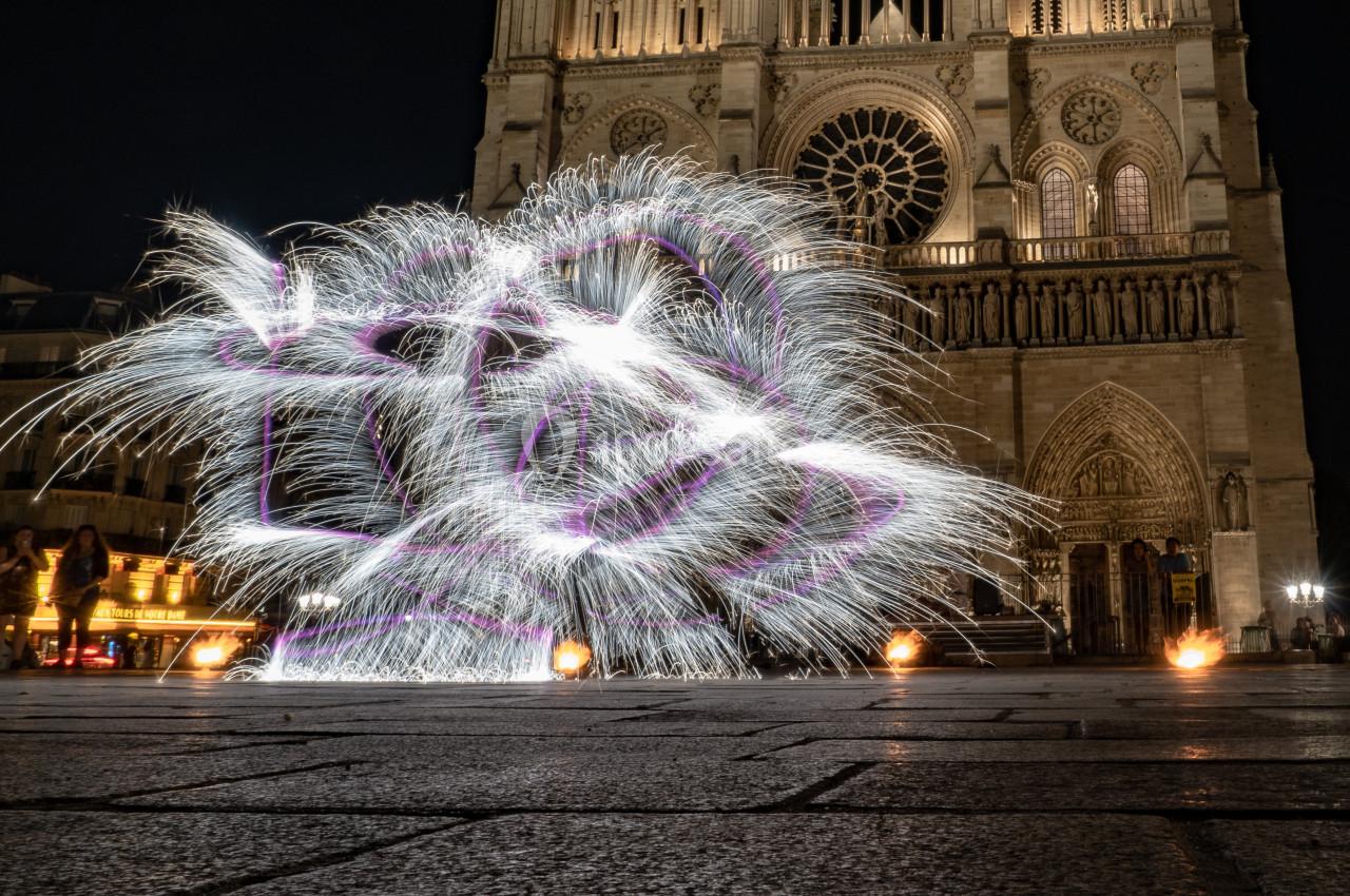 Spectacle de jonglage lumineux devant une cathédrale illuminée la nuit, avec des flammes au sol.
