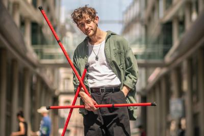 Un jongleur manipule des bâtons rouges dans une galerie lumineuse avec une verrière en arrière-plan.