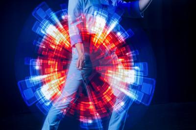 Un jongleur réalise une performance avec des bâtons rouges dans une galerie lumineuse bordée de colonnes.