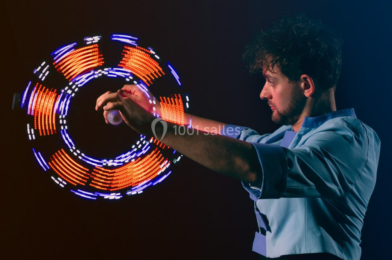 Un homme jongle avec des objets lumineux créant des motifs circulaires colorés dans un environnement sombre.