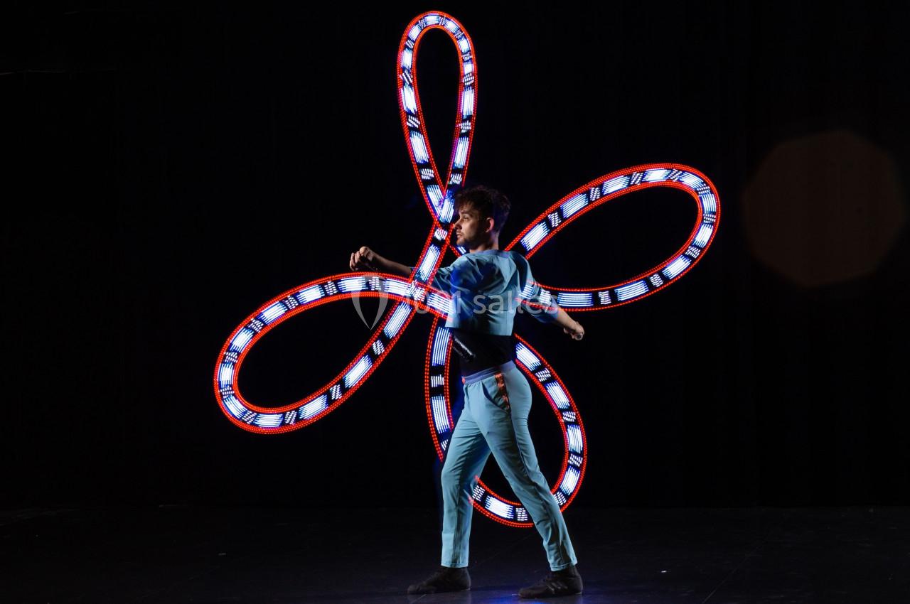 Un artiste jongle avec des anneaux lumineux formant des motifs colorés sur une scène sombre.