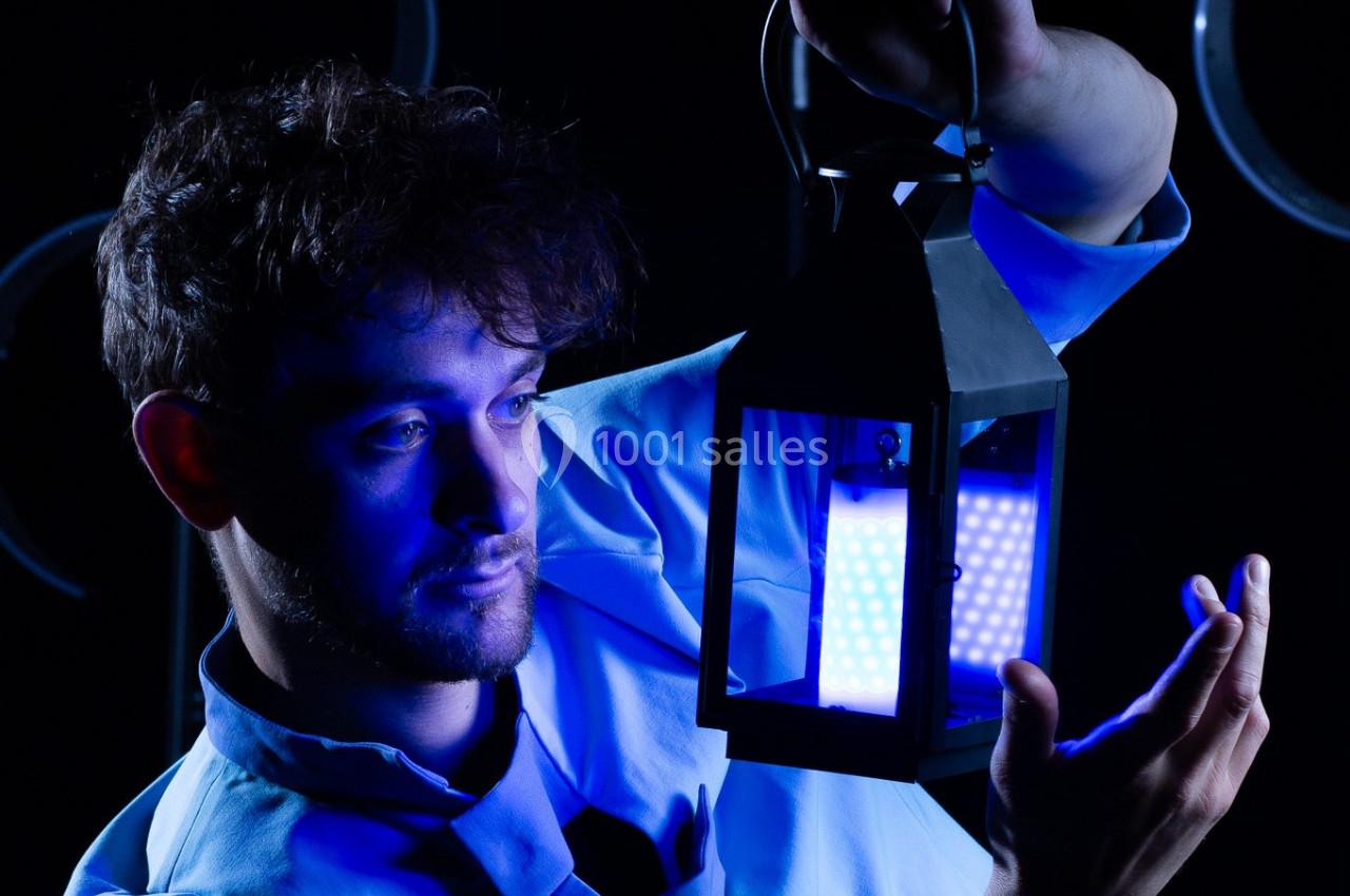 Un homme en blouse blanche tient une lanterne émettant une lumière bleue dans un environnement sombre.
