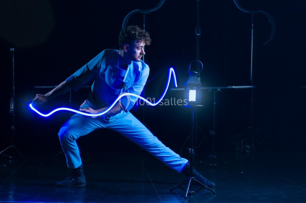 Un homme en mouvement manipule une lumière bleue lumineuse dans un environnement sombre et artistique.