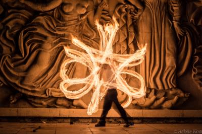 Un jongleur réalise une performance avec des bâtons rouges dans une galerie lumineuse bordée de colonnes.