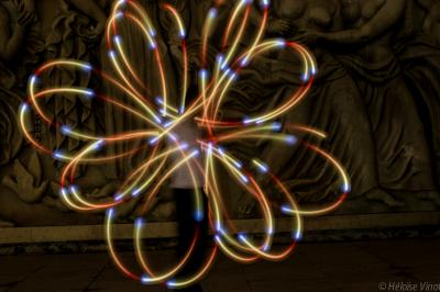 Un jongleur réalise une performance avec des bâtons rouges dans une galerie lumineuse bordée de colonnes.