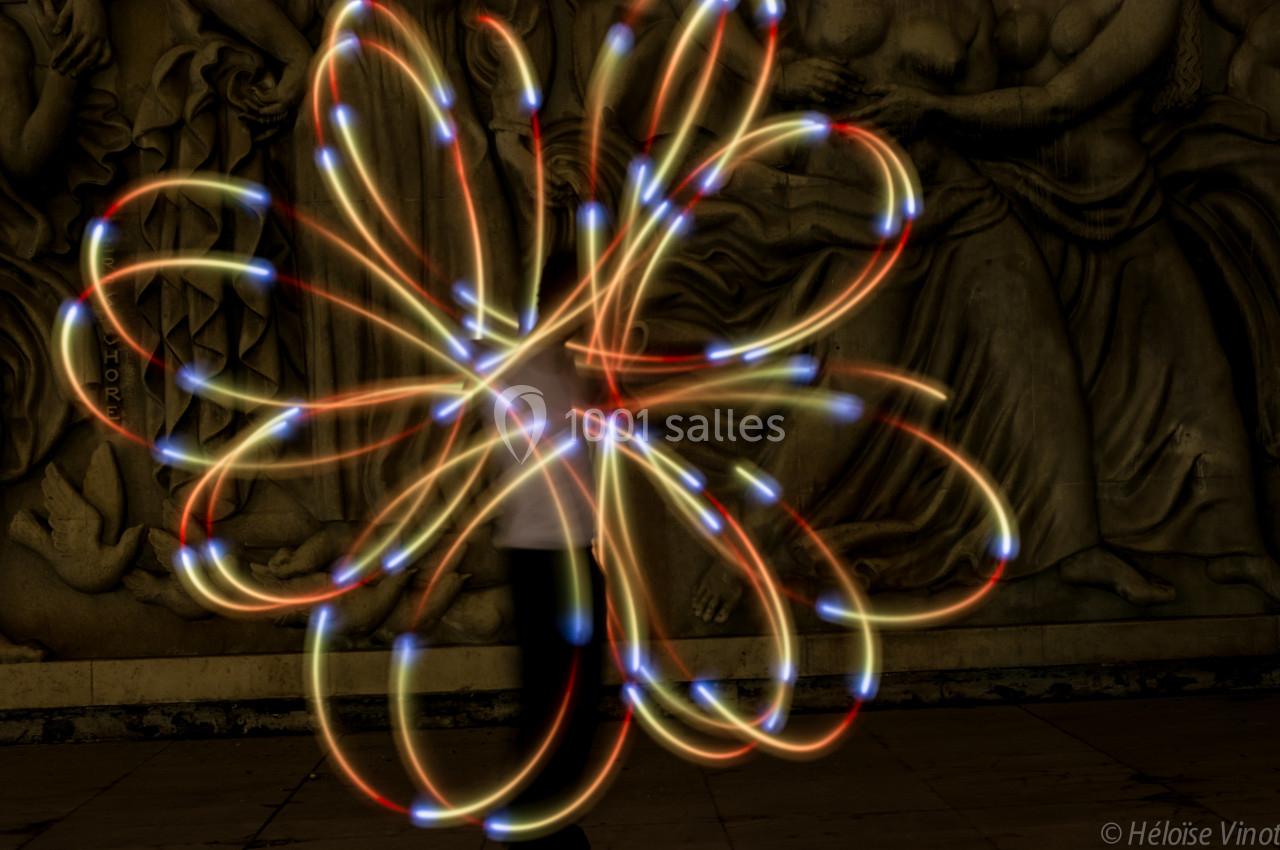 Personne manipulant des lumières colorées en mouvement, créant des motifs lumineux devant une fresque sculptée.