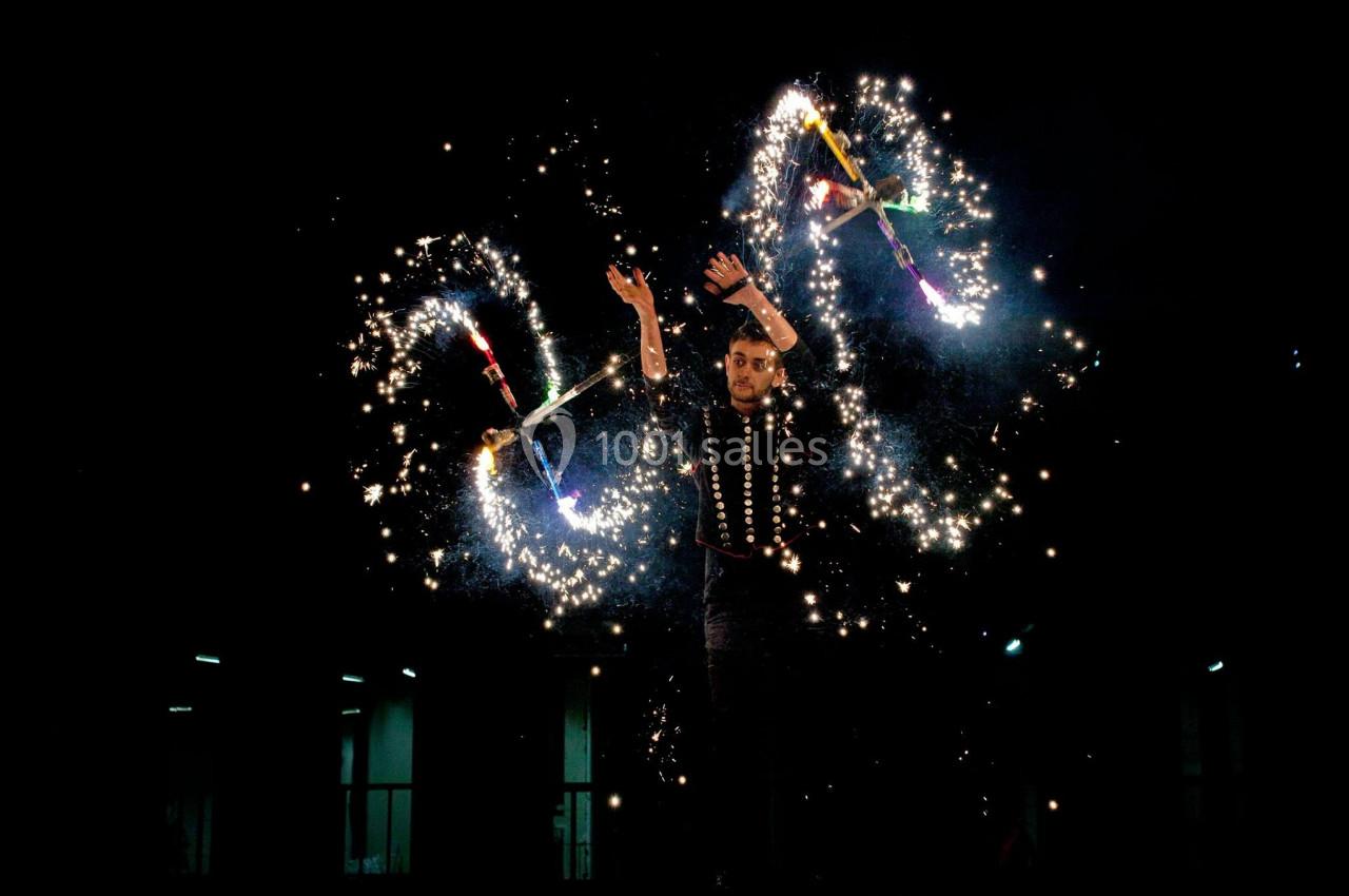 Un jongleur manipule des bâtons enflammés produisant des étincelles dans l'obscurité.