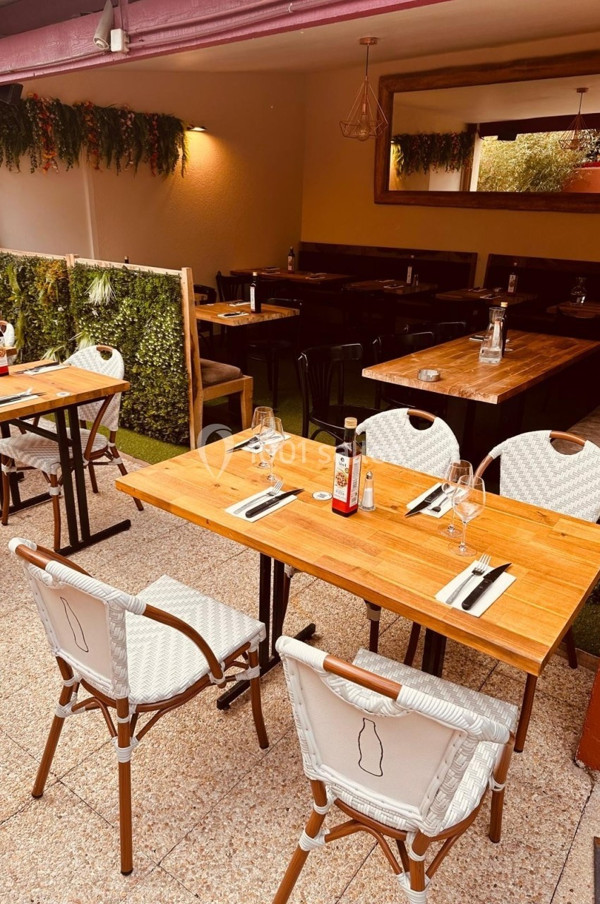 Terrasse d'un restaurant avec tables en bois, chaises blanches et décoration végétale sur les murs.