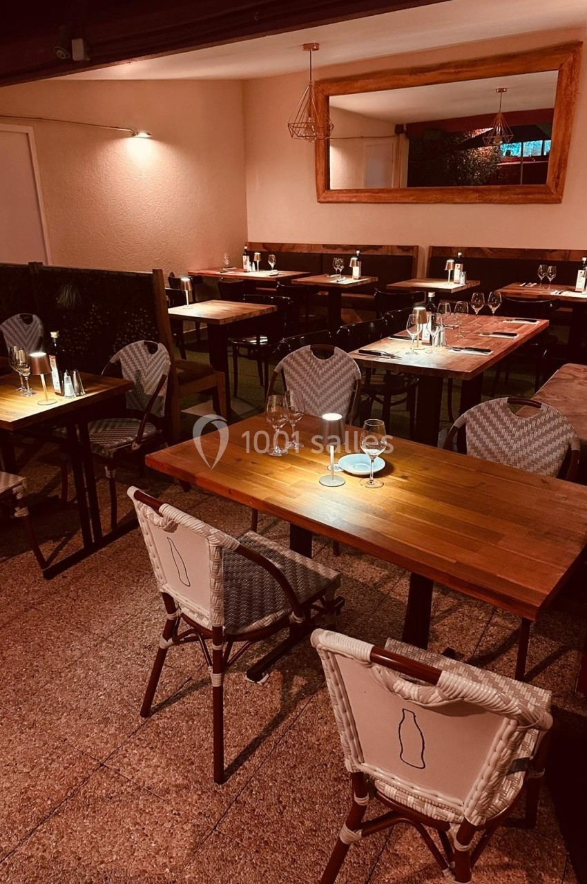 Salle de restaurant avec tables en bois, chaises tressées et éclairage tamisé, ambiance chaleureuse et intime.