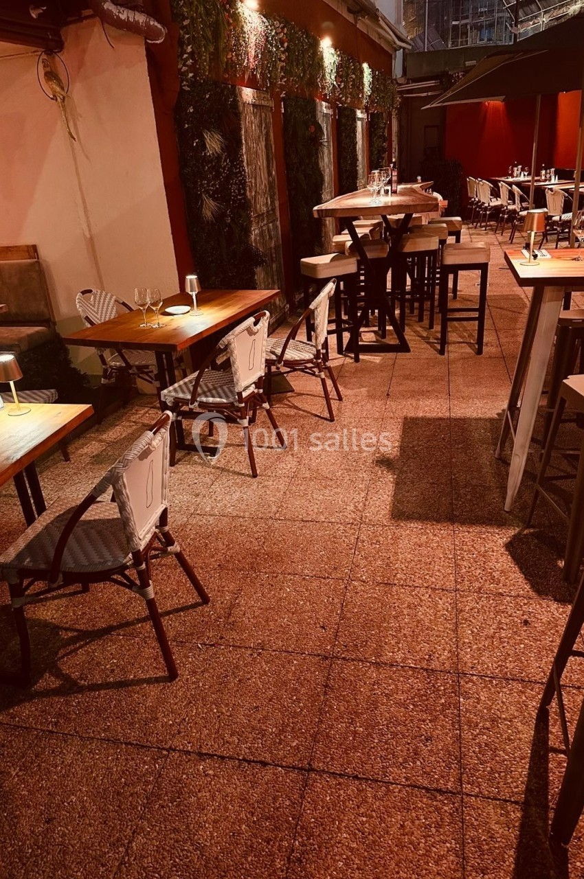 Terrasse extérieure d'un restaurant avec tables en bois, chaises et éclairage tamisé en soirée.