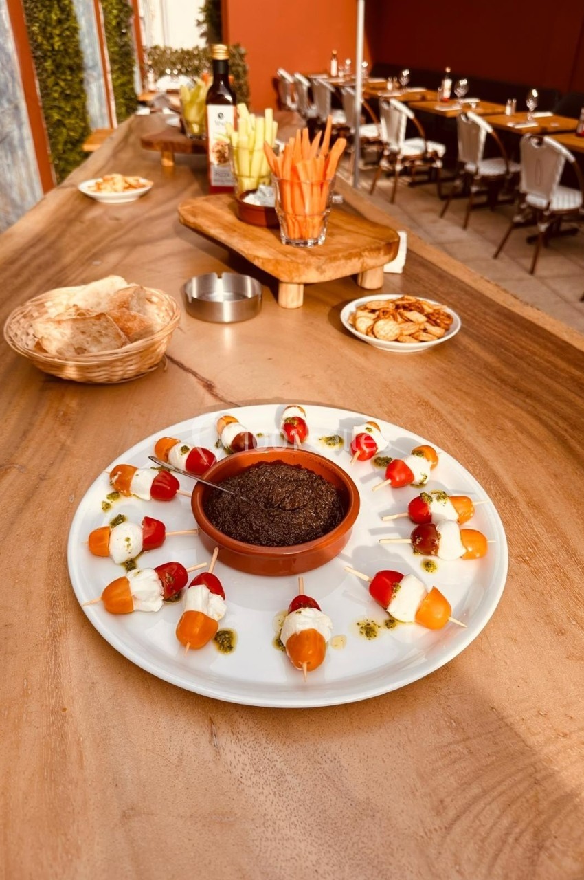 Assiette de brochettes apéritives avec tomates, mozzarella et pesto, accompagnée d'une sauce dans un bol au centre.