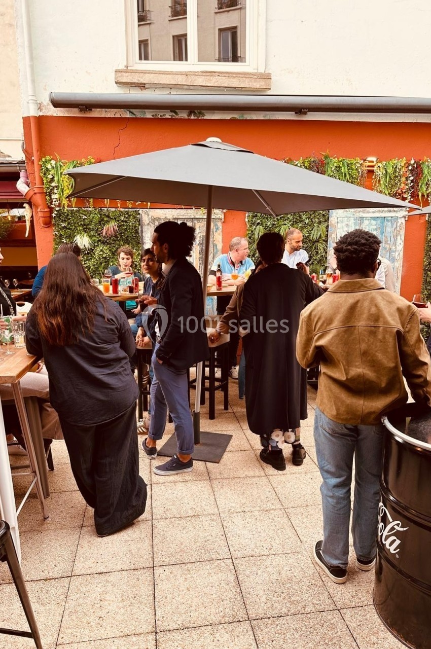 Groupe de personnes discutant et partageant un moment convivial sur une terrasse extérieure avec parasol.