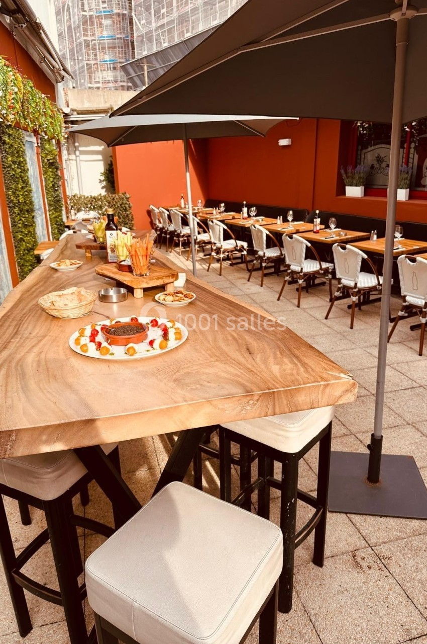 Terrasse aménagée avec une grande table en bois, des chaises, des parasols et des plats disposés pour un repas convivial.
