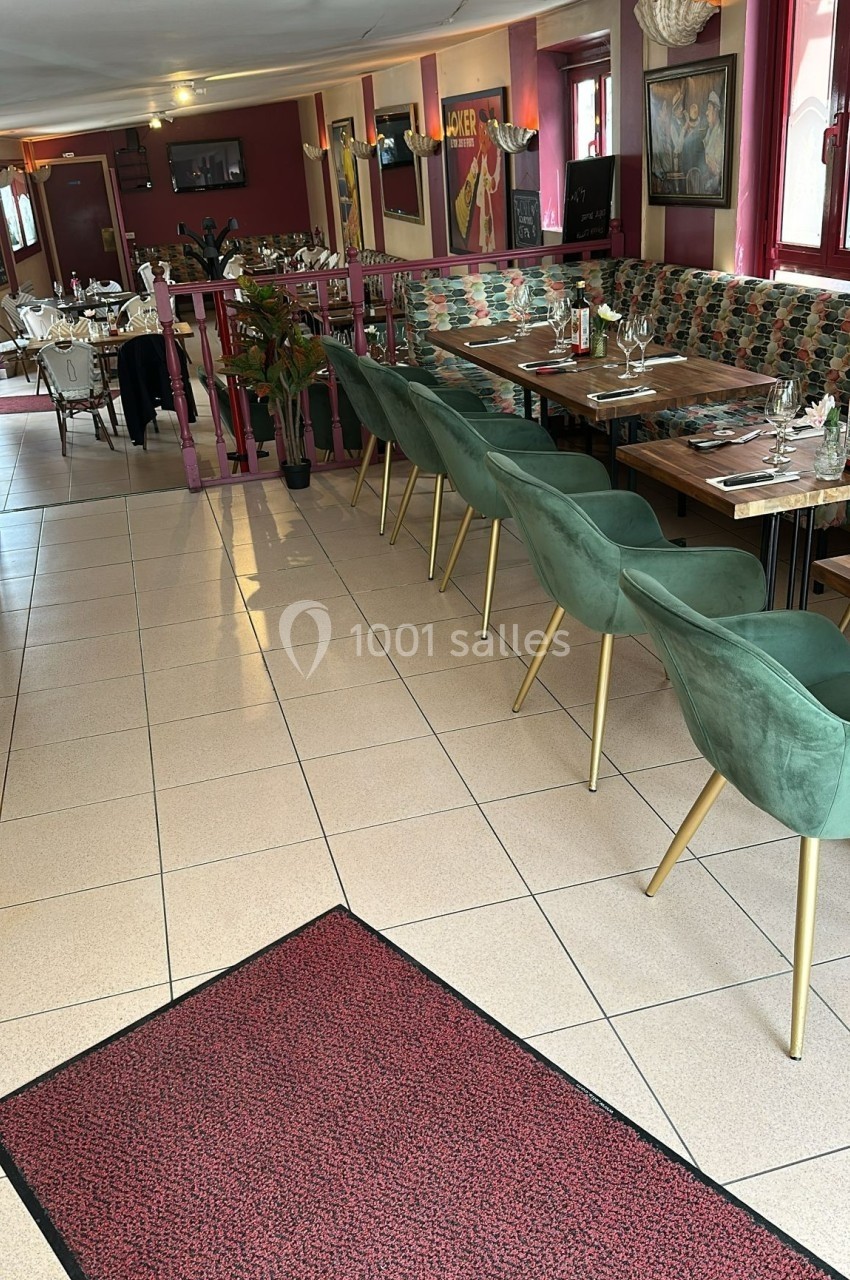 Salle de restaurant avec tables dressées, chaises vertes et décoration intérieure aux tons rouges et verts.