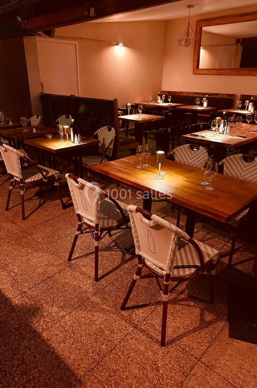 Salle de restaurant avec tables en bois, chaises en rotin et éclairage tamisé créant une ambiance chaleureuse.
