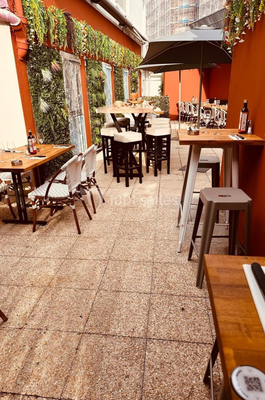 Terrasse extérieure avec tables en bois, chaises, parasol et mur végétalisé dans un cadre chaleureux.
