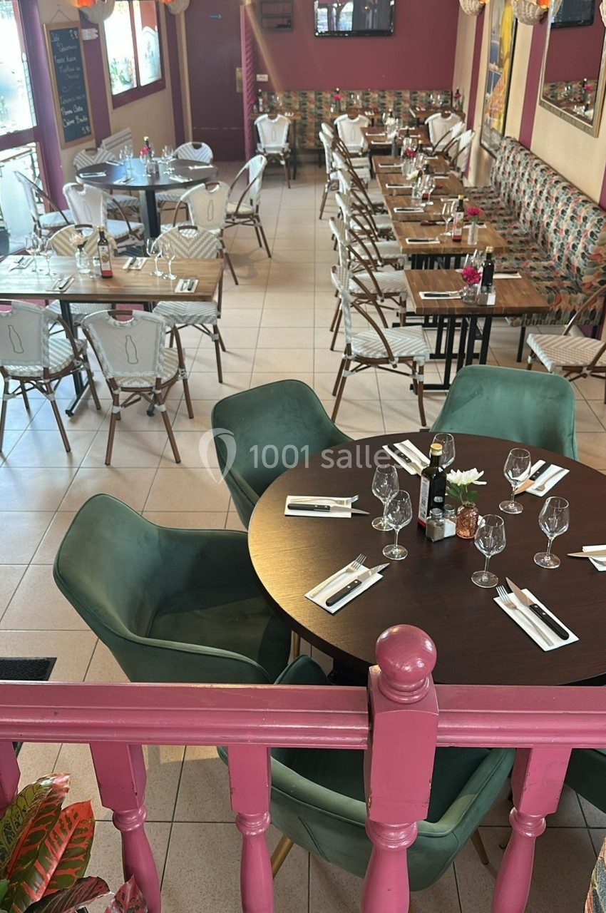 Salle de restaurant lumineuse avec tables dressées, chaises variées et décoration chaleureuse dans des tons rouges et verts.
