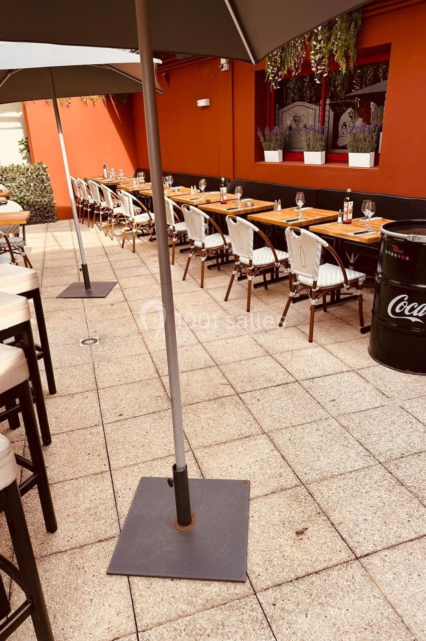 Terrasse extérieure avec tables et chaises alignées, parasols ouverts et mur rouge en arrière-plan.