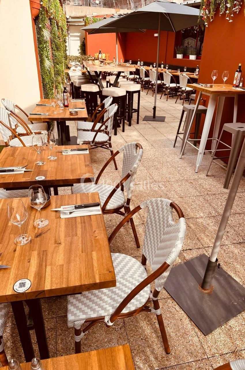 Terrasse d'un restaurant avec tables en bois, chaises tressées et parasols, dans un cadre extérieur ensoleillé.