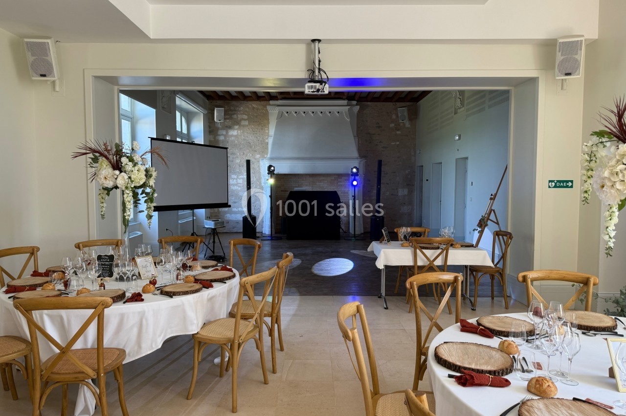 Salle de réception décorée avec des tables dressées, un projecteur, un écran et une piste de danse éclairée.