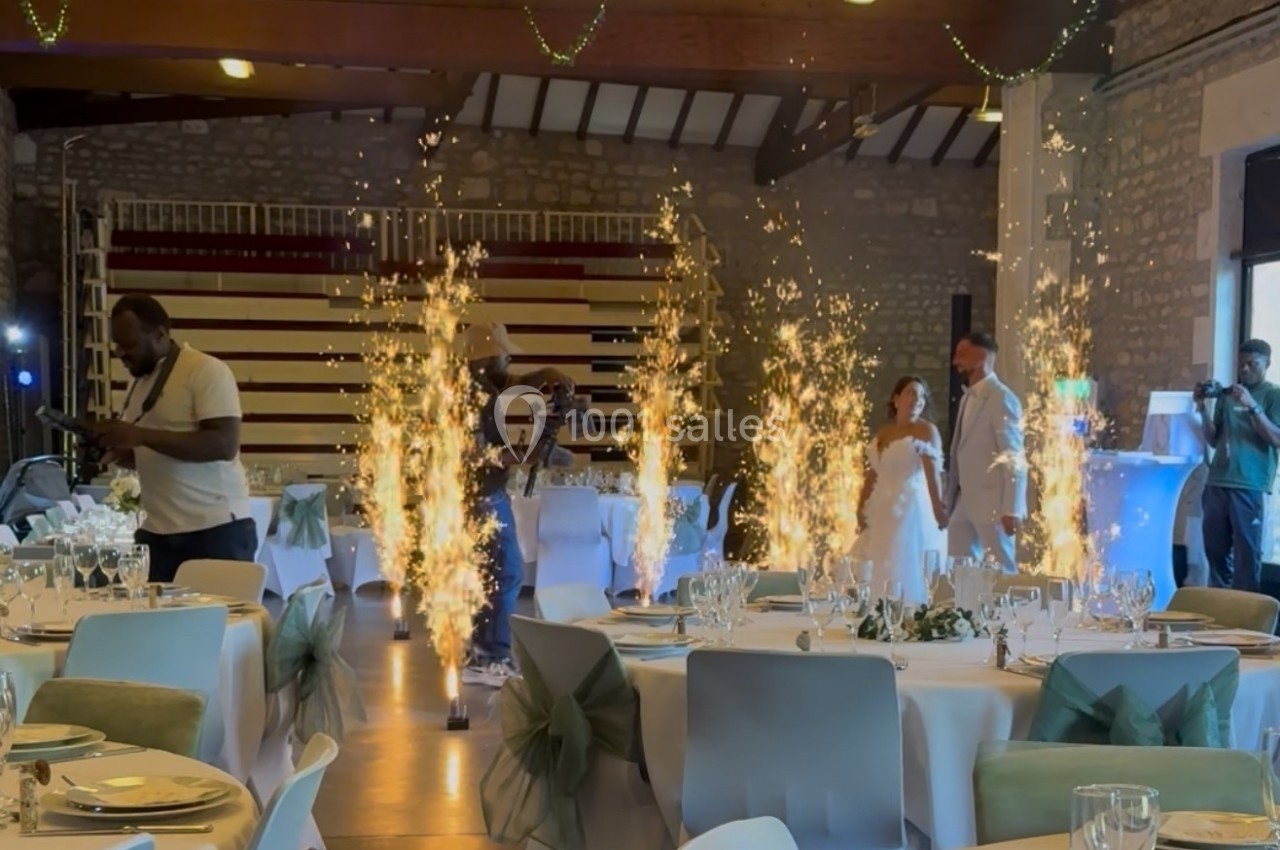 Mariés entrant dans une salle de réception décorée, entourés de fontaines lumineuses et de tables dressées.