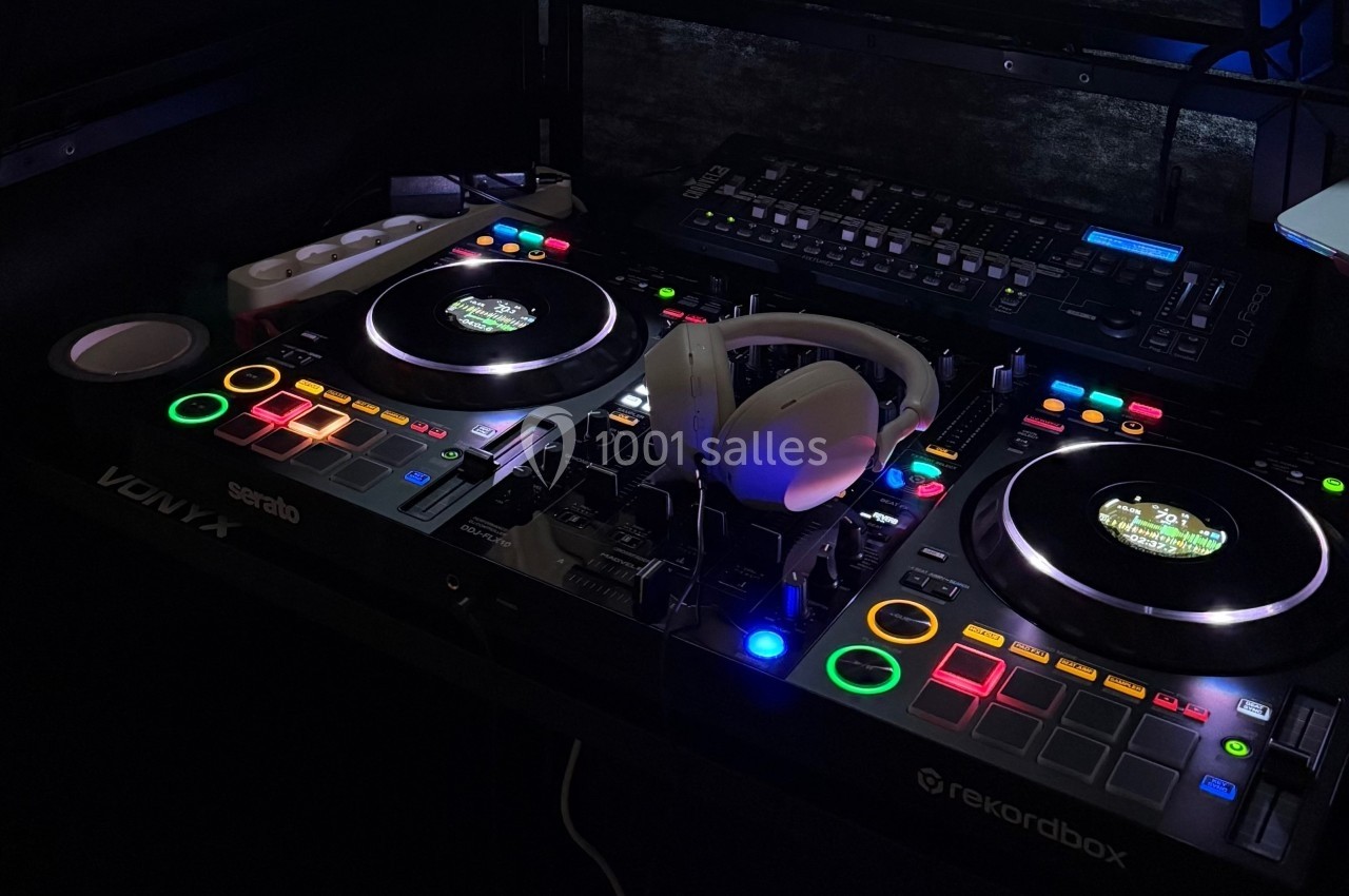 Table de mixage DJ avec platines lumineuses, casque audio posé au centre et équipement électronique en arrière-plan.