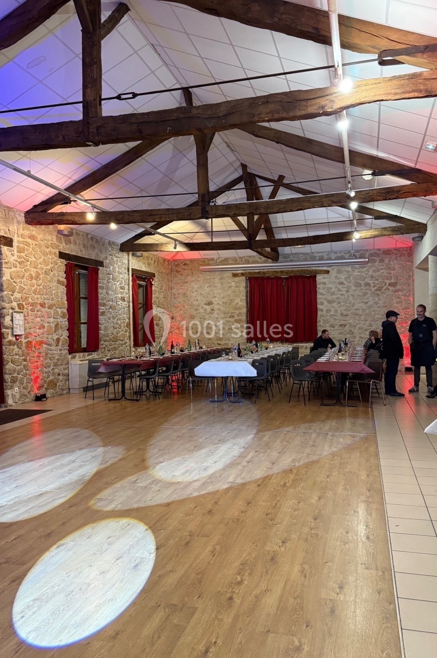 Salle de réception avec murs en pierre, poutres apparentes, tables dressées et éclairage tamisé.