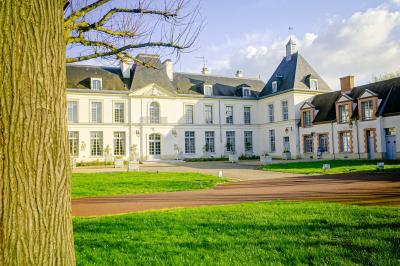 Statue de sphinx en pierre posée sur un socle, entourée de végétation et d'une haie dans un jardin.
