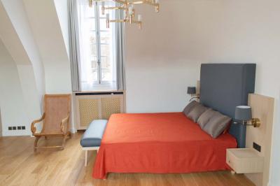 Statue de sphinx en pierre posée sur un socle, entourée de végétation et d'une haie dans un jardin.