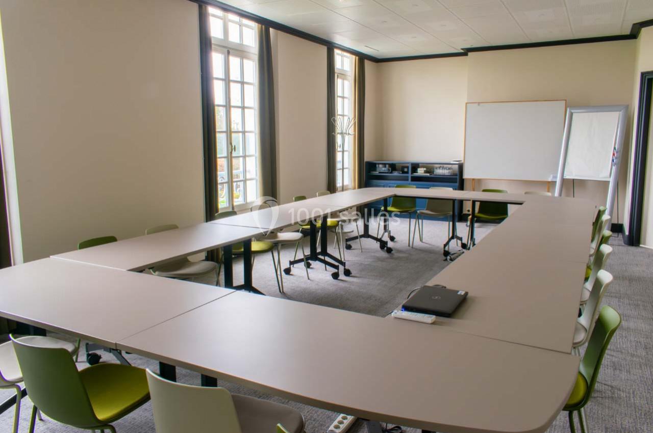 Salle de réunion lumineuse avec des tables disposées en U, des chaises colorées et un tableau blanc au fond.