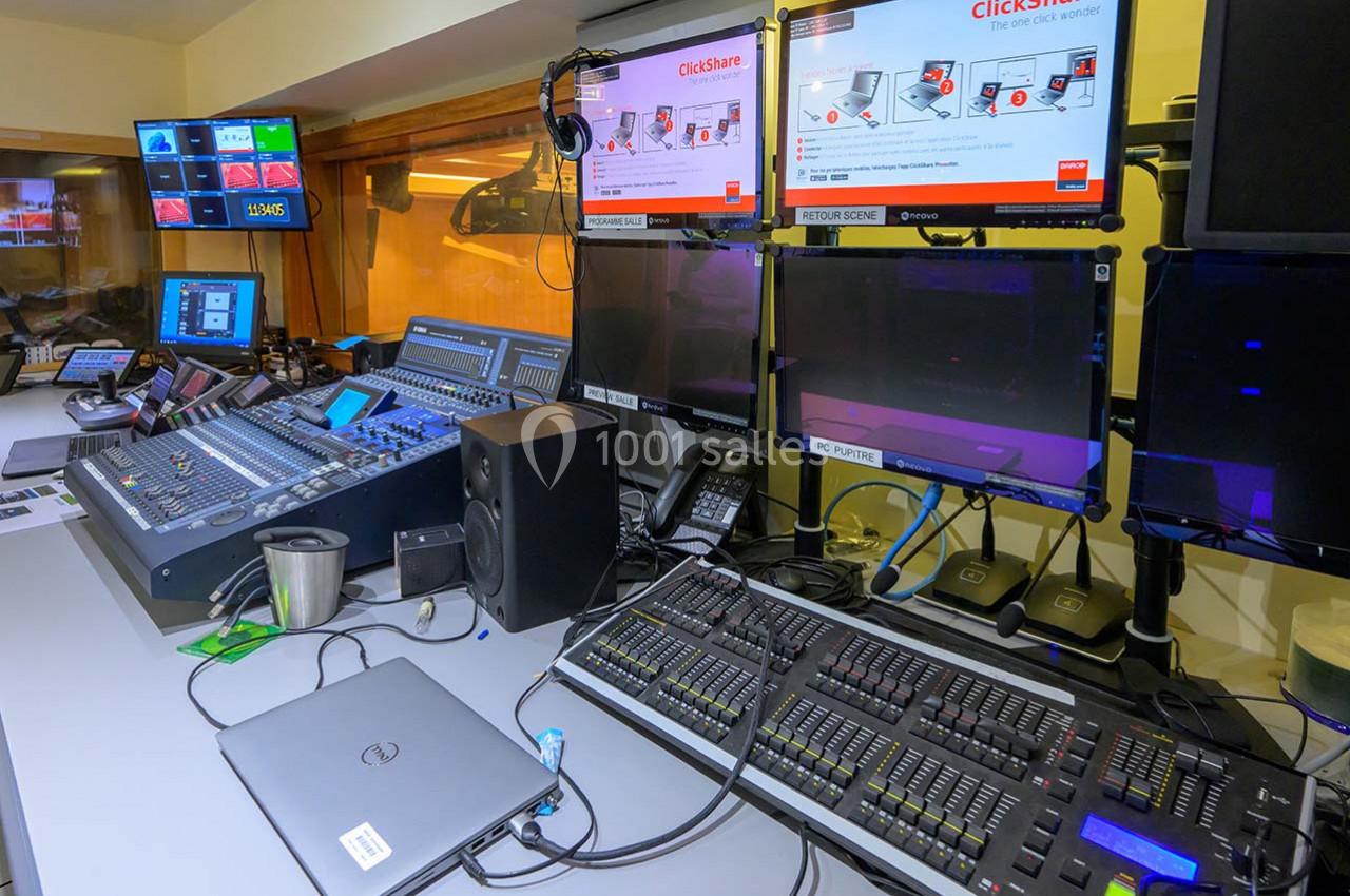 Poste de contrôle audiovisuel avec consoles de mixage, écrans, ordinateurs et équipements techniques dans une salle.