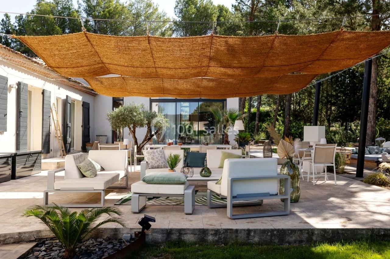 Terrasse aménagée avec mobilier de jardin moderne, ombragée par une grande toile en fibre naturelle, entourée de verdure.