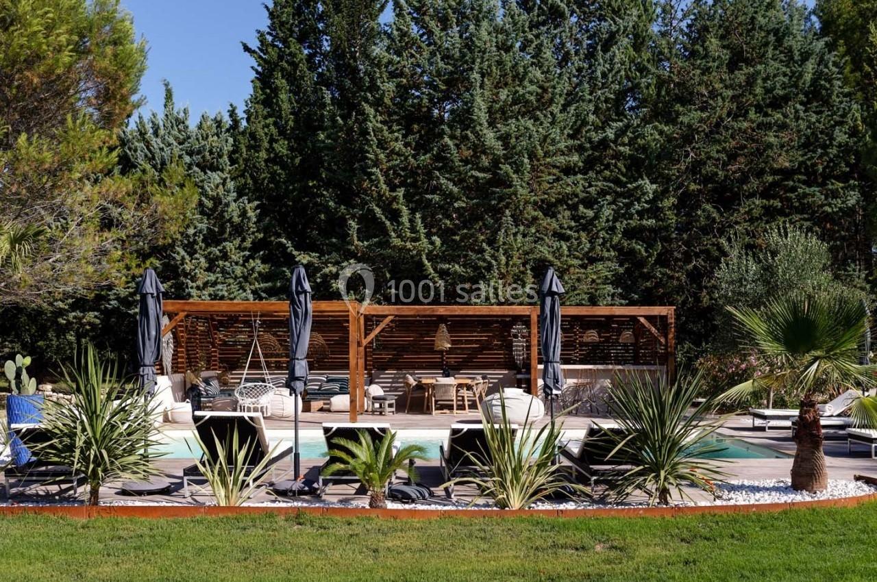 Terrasse avec piscine entourée de végétation, mobilier d'extérieur sous une pergola en bois et parasols noirs.