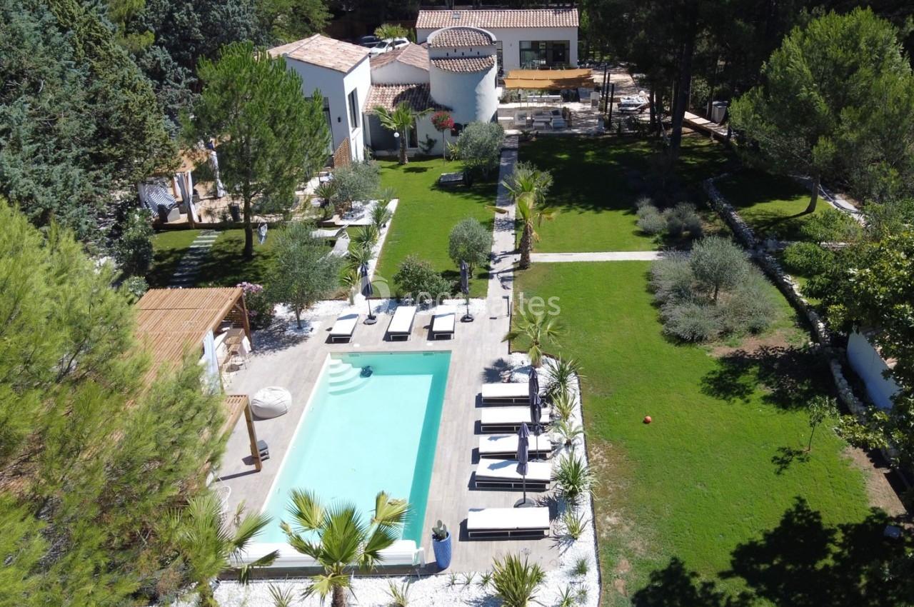 Vue aérienne d'une propriété avec piscine, transats, pelouse bien entretenue et bâtiments entourés de végétation.