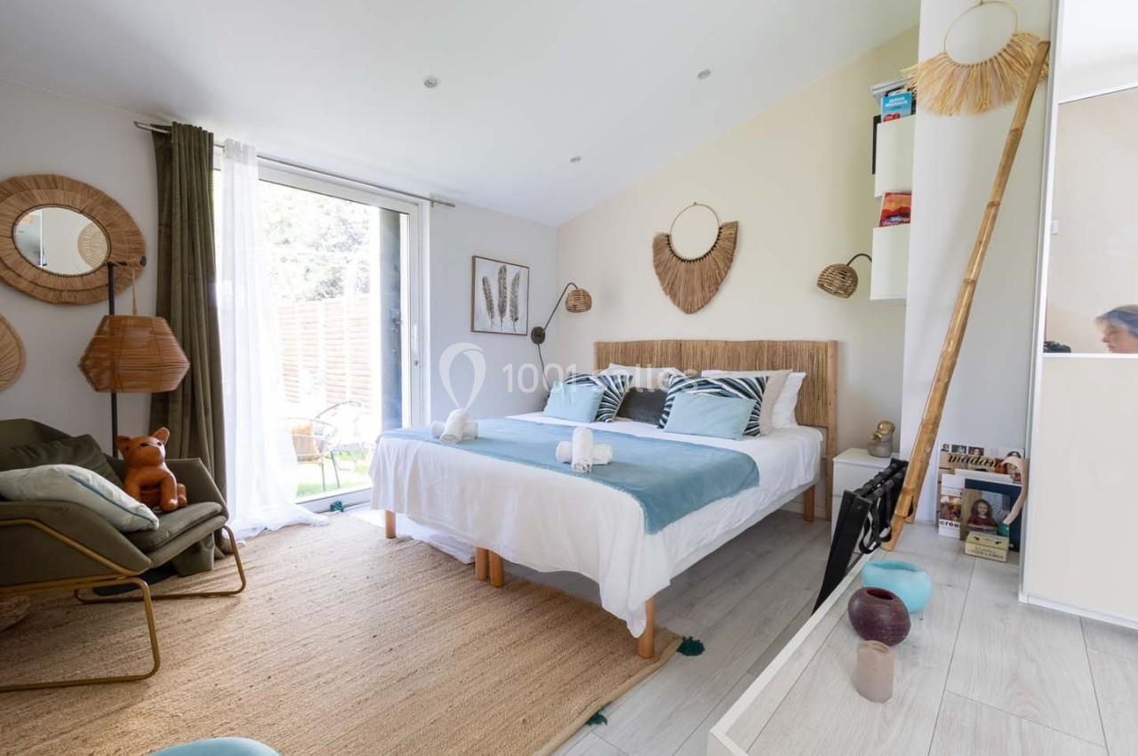 Chambre lumineuse avec lit double, décoration naturelle en rotin, fauteuil, et accès à une terrasse extérieure.