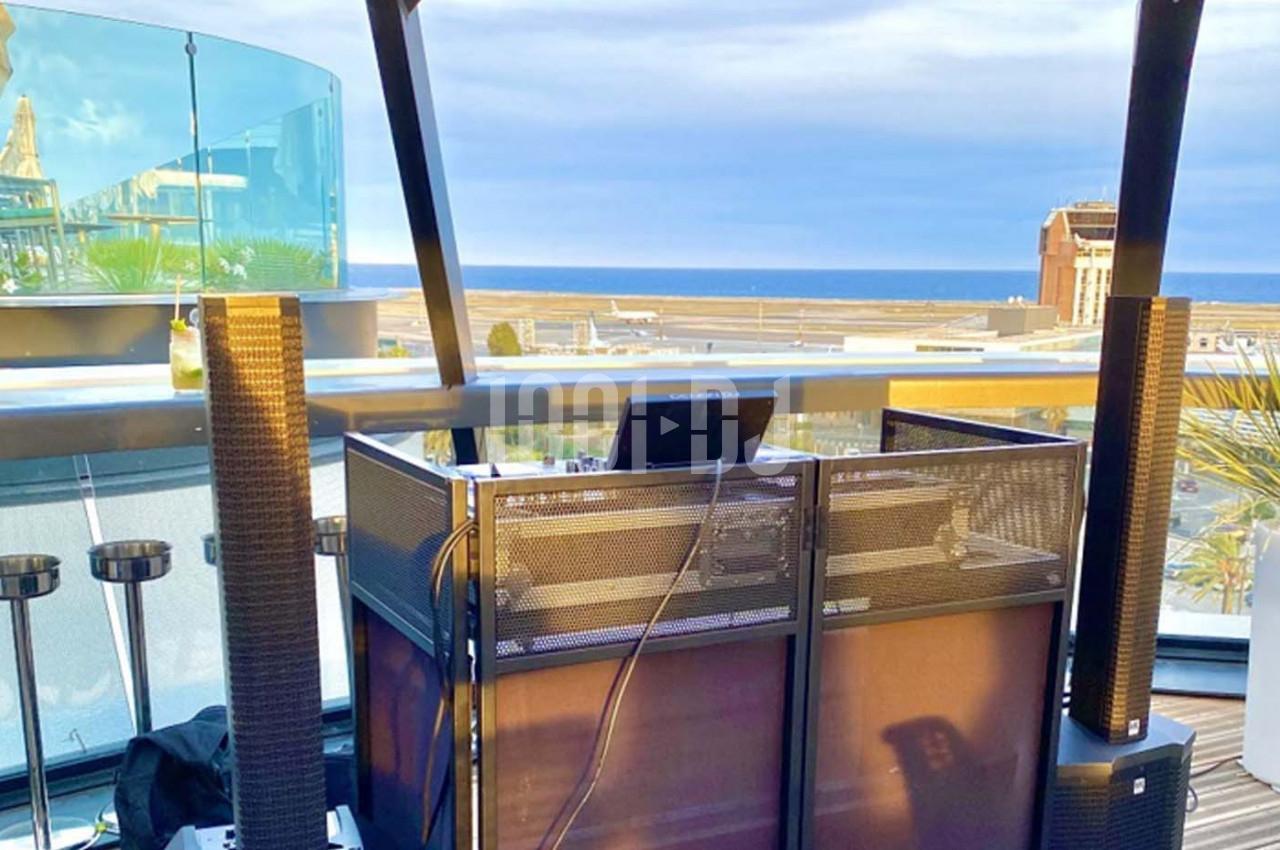 Poste de DJ installé sur une terrasse avec vue sur la mer et un ciel partiellement nuageux.