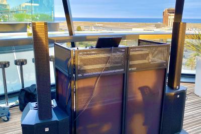 Miniature DJ Mougins (Alpes-Maritimes) - Dj Art Winder #12 Console de DJ avec enceintes sur une terrasse en hauteur, offrant une vue sur la mer et des bâtiments en arrière-plan.