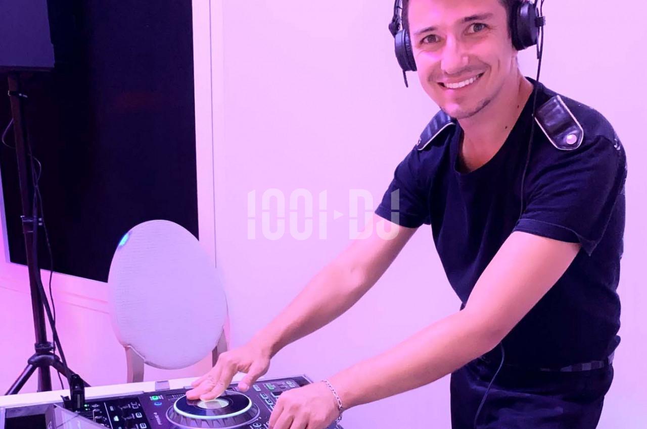 Un DJ souriant mixe de la musique sur une table de mixage dans un environnement éclairé en rose.