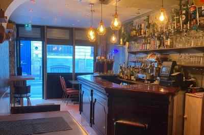 Miniature Location salle Paris 11 (Paris) - Bar de l'Hôtel de la Paix #10 Façade d'un café avec une table extérieure en bois, revêtement en gazon synthétique et intérieur éclairé visible.