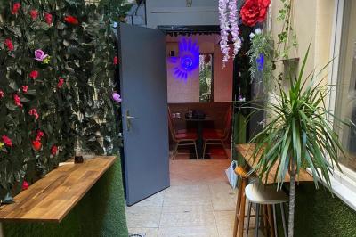 Miniature Location salle Paris 11 (Paris) - Bar de l'Hôtel de la Paix #13 Façade d'un café avec une table extérieure en bois, revêtement en gazon synthétique et intérieur éclairé visible.