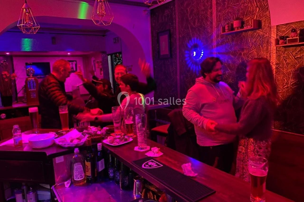 Des personnes discutent et dansent dans un bar à l'ambiance tamisée avec des lumières colorées.